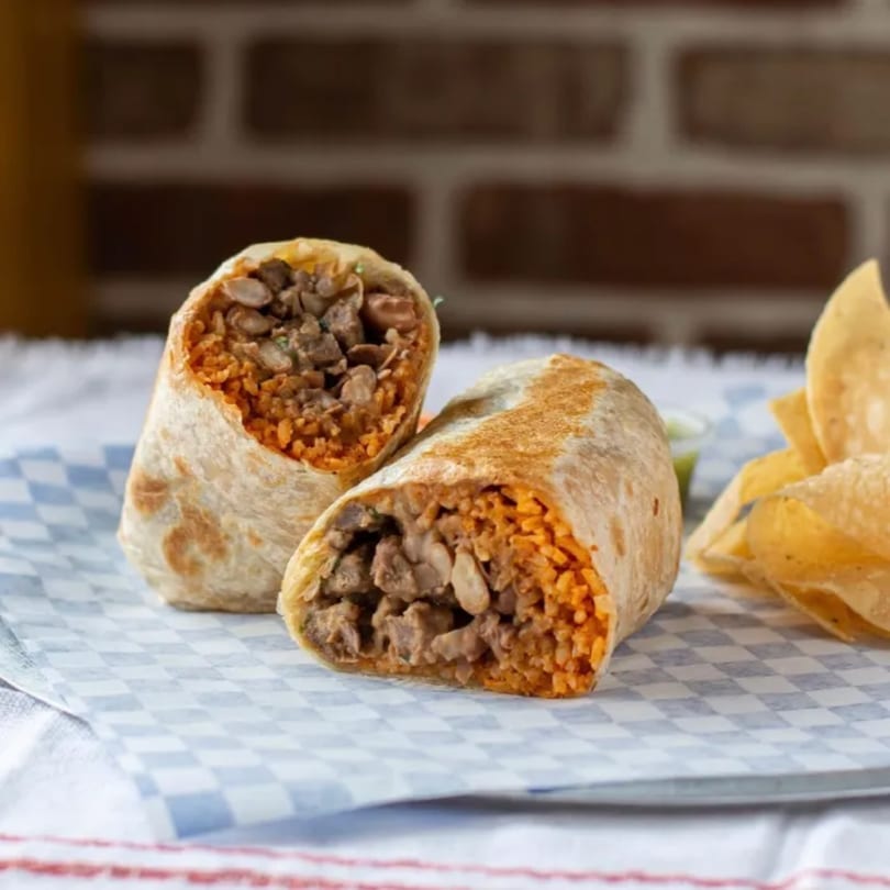 Two halves of a Somos Oaxaca burrito filled with meat and rice, served with tortilla chips.